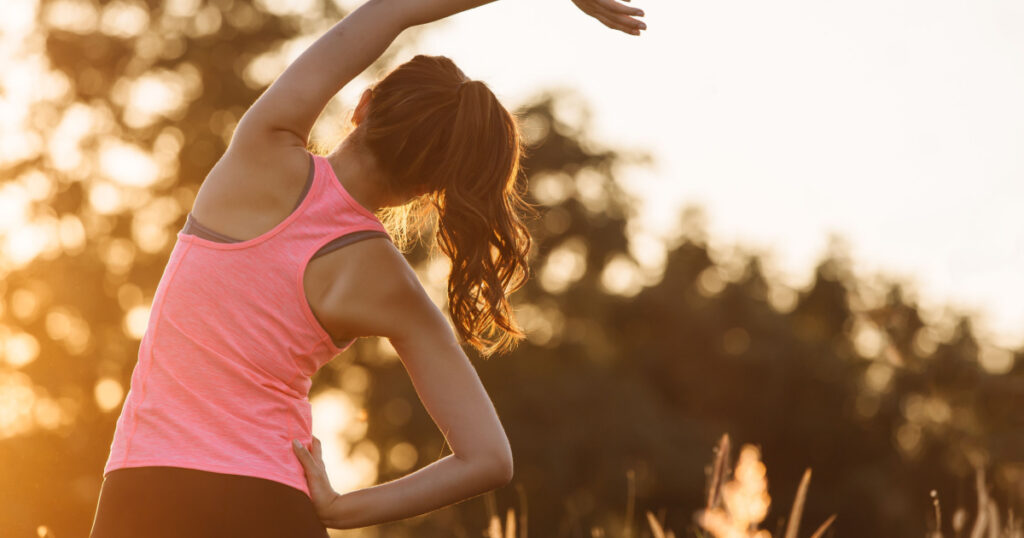 Young female workout before fitness training session at the park. Healthy young woman warming up outdoors