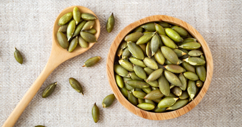 Pumpkin seeds in wooden bowl and spoon, top view