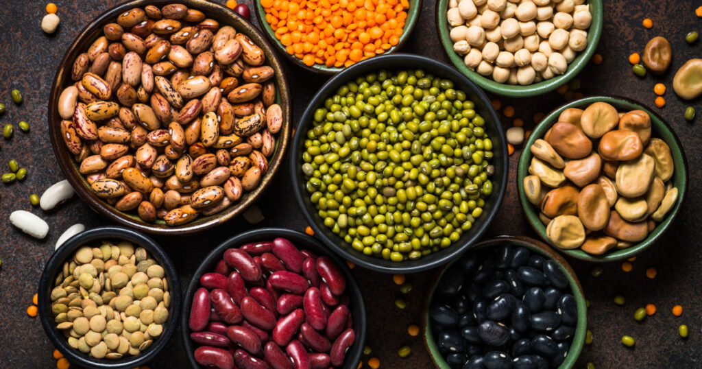 Legumes, lentils, chikpea and beans assortment in different bowls on stone table. Top view.
