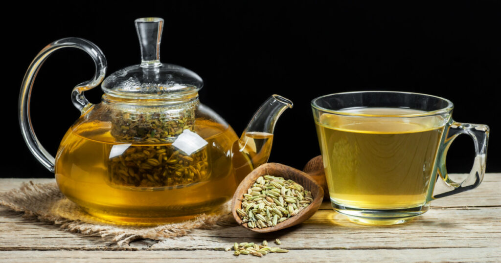 Herbal infusion fennel tea in glass cup and glass tea pot with dried fennel seeds in wooden shovel. Herbal tea alternative medicine background concept.