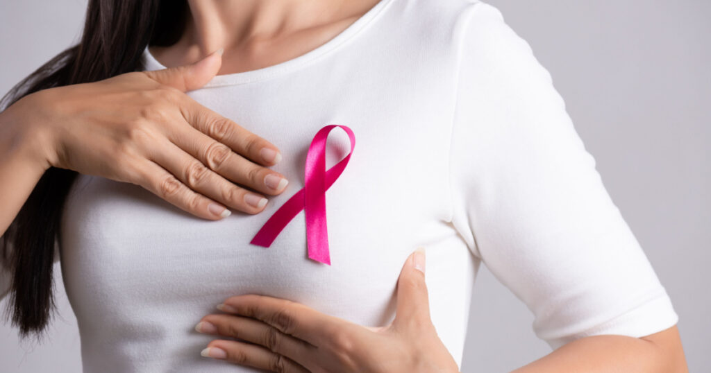 Closeup of pink badge ribbon on woman chest to support breast cancer cause. Healthcare, medicine and breast cancer awareness concept.