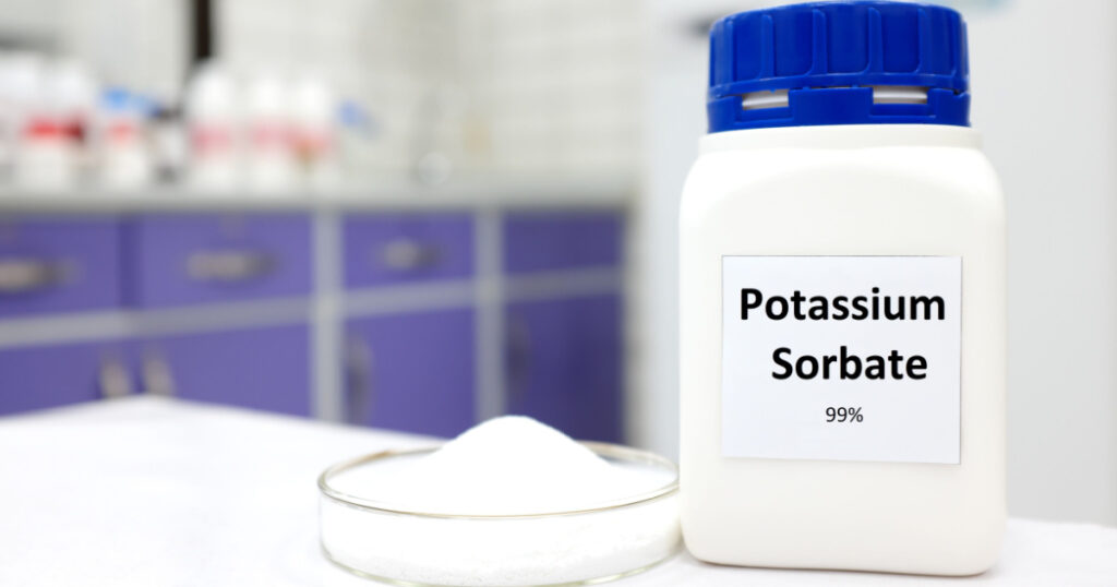 Selective focus of bottle of pure potassium sorbate food additive beside a petri dish with white solid powder substance. White laboratory background with copy space.