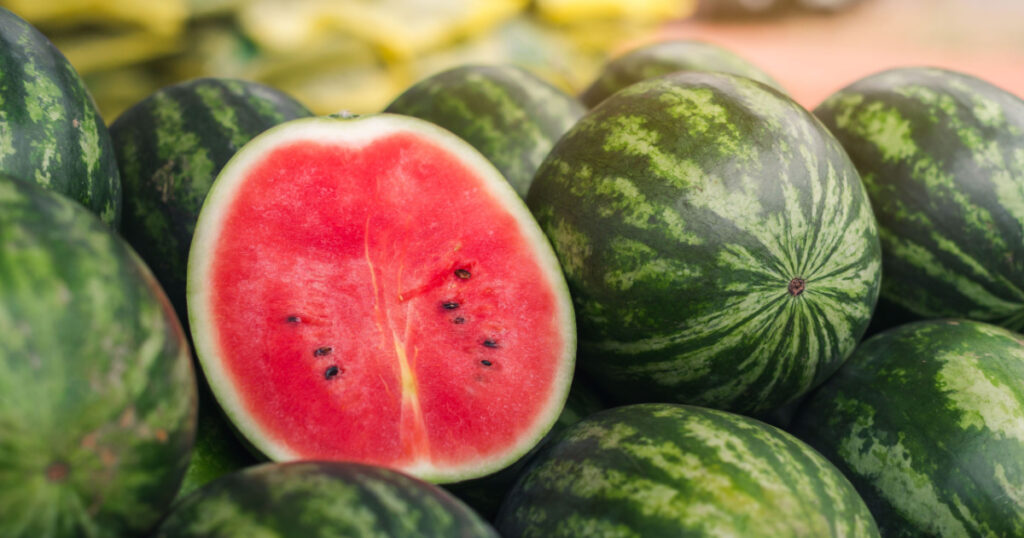 Several large sweet green watermelons and cut watermelons, several large sweet green watermelons are placed on a wooden table on a natural background for sale.
