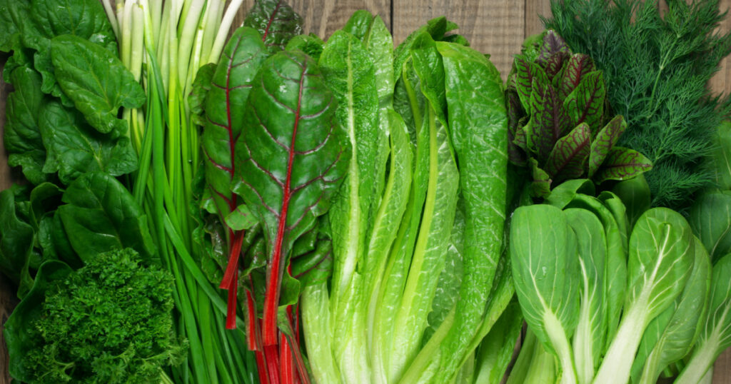 Spring vitamin weight loss foods set of various green leafy vegetables on rustic wooden table. Top view point.
