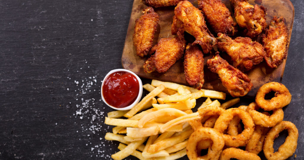 fast food products : onion rings, french fries and fried chicken on dark table, top view