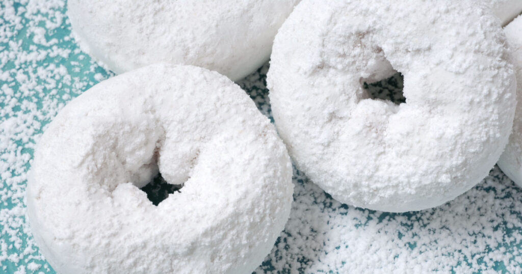 Powdered sugar mini donuts on a ceramic plate with extra sugar sprinkled all around. Macro with shallow dof