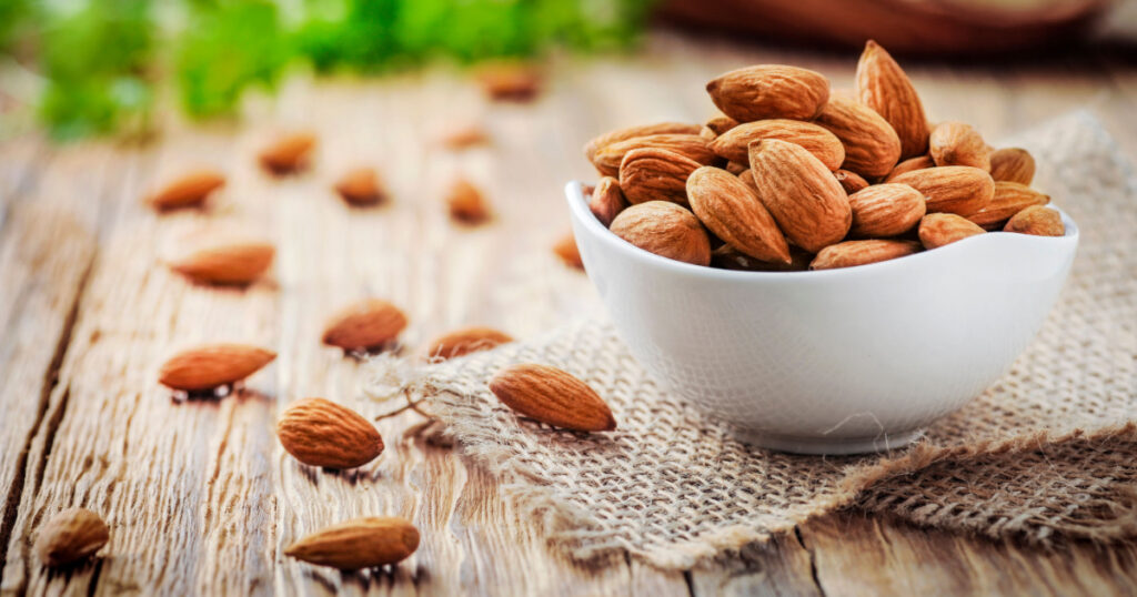 Almonds in white porcelain bowl on wooden table. Almond concept with copyspace.