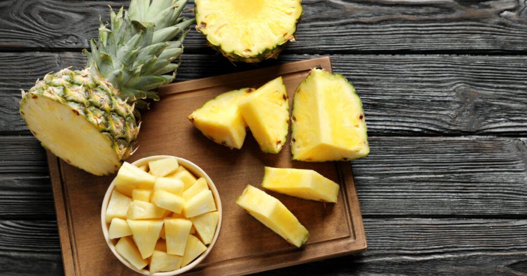 Wooden board with fresh sliced pineapple on table, top view