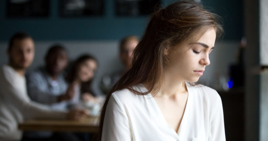 Sad young woman avoiding ignoring bad friends suffering from gossiping, bullying, unfair attitude or discrimination, frustrated millennial girl feeling upset, hurt and offended sitting alone in cafe