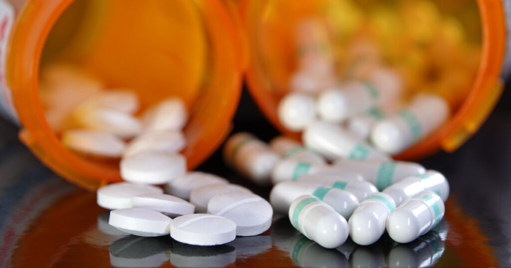 Medication overuse or adverse drug interaction concept - two types of prescription drugs spilling from containers
