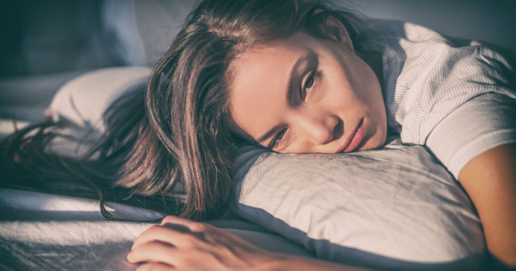 Tired woman lying in bed can't sleep late at night with insomnia. Asian girl with funny face sick or sad depressed sleeping at home.