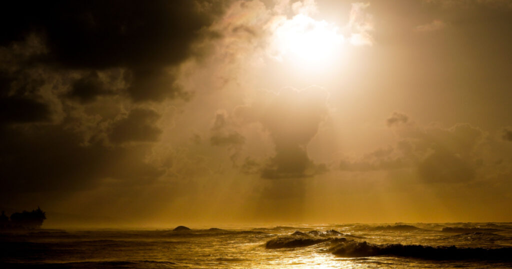 Angry seas at sunset and crashing waves on rocks with sun rays through cloudy skies God Rays Faith Hope danger powerful nature heavy seas blue oceans orange skies blue and aqua waters rocky shores