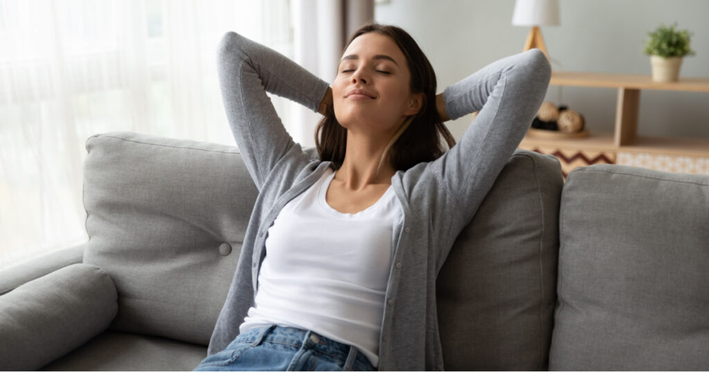 Relaxed serene pretty young woman feel fatigue lounge on comfortable sofa hands behind head rest at home, happy calm lady dream enjoy wellbeing breathing fresh air in cozy home modern living room
