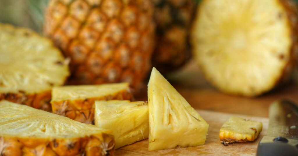 Close up at piece of Pineapple(Ananas comosus) on wooden table with blurred half,sliced and whole background.Sweet,sour and juicy taste.Have a lot of fiber,vitamins C and minerals.Food,Fruit concept.