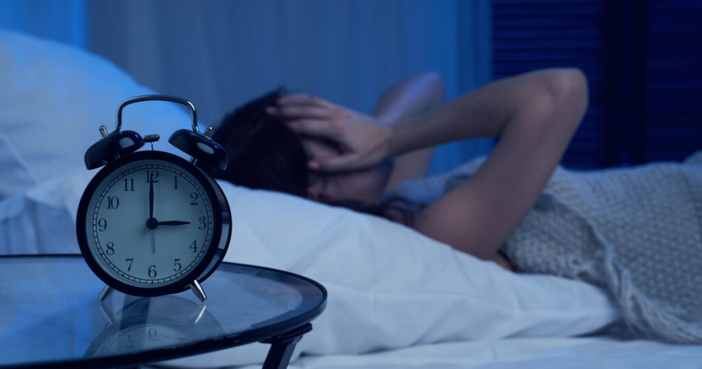 Unhappy woman with insomnia lying on bed next to alarm clock at night