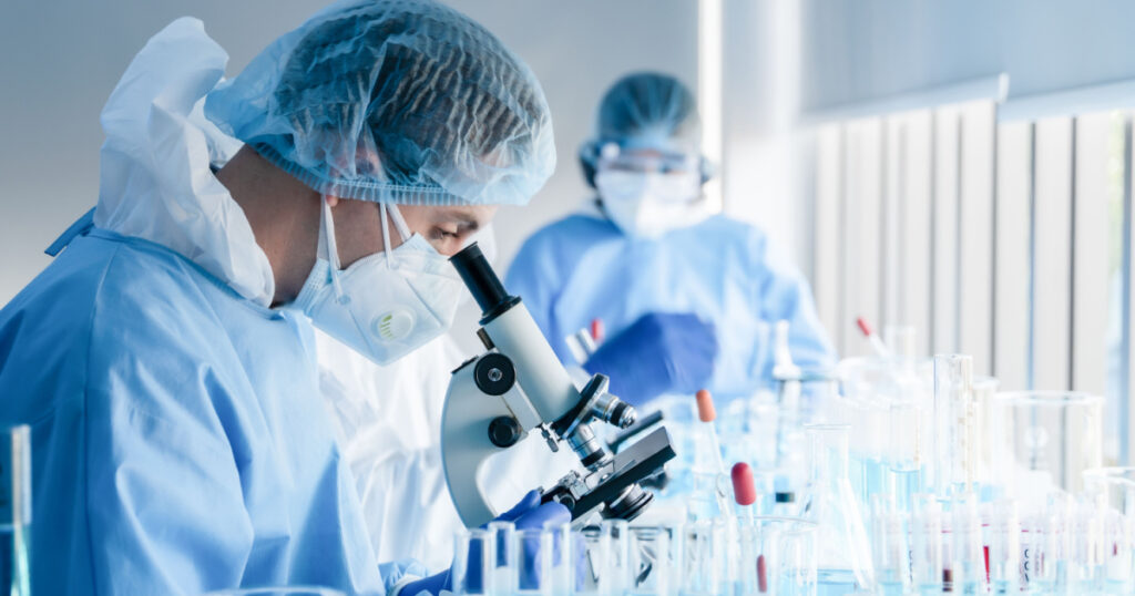 biochemical research scientist team working with microscope for coronavirus vaccine development in pharmaceutical research labolatory, selective focus
