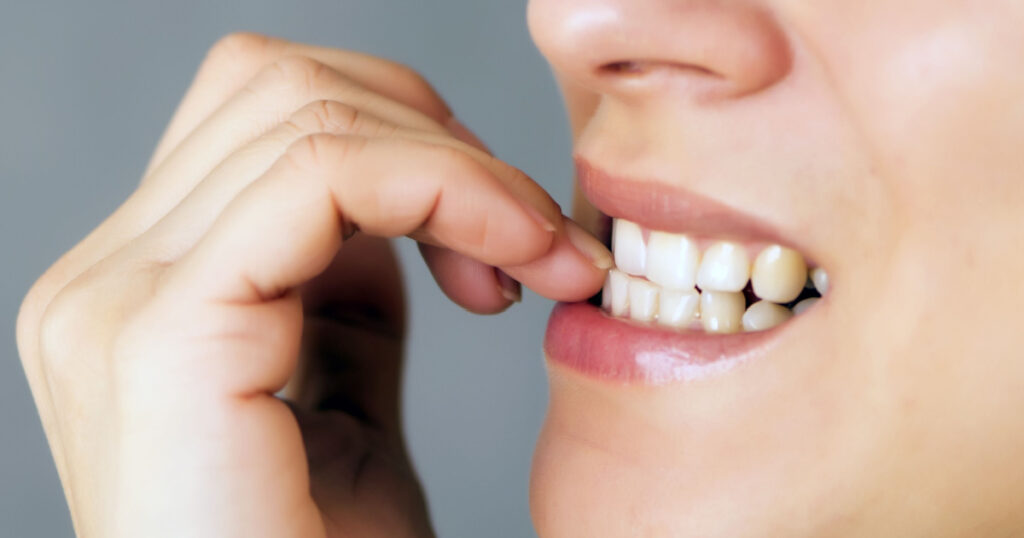 nervous young woman biting her nails on gray background
