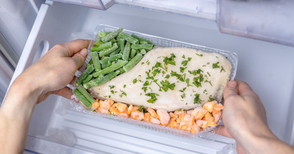 Women's hands are taking out a container with a frozen dish from the freezer of the fridge. Concept of a fast dinner cooking and time saving.
