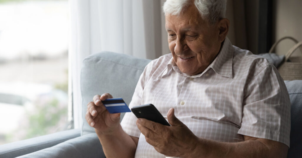 Focused man using mobile phone and making online payment by credit card. Customer shopping from home, paying for purchase on Internet stores, using banking or ecommerce app for transactions
