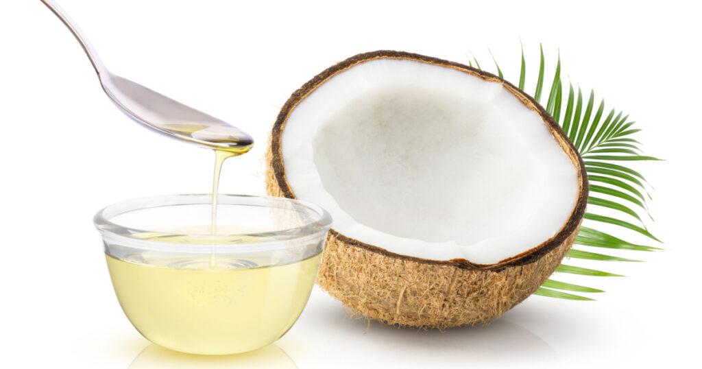 Coconut oil in glass bowl and coconut fruit with green leaves isolated on white background.