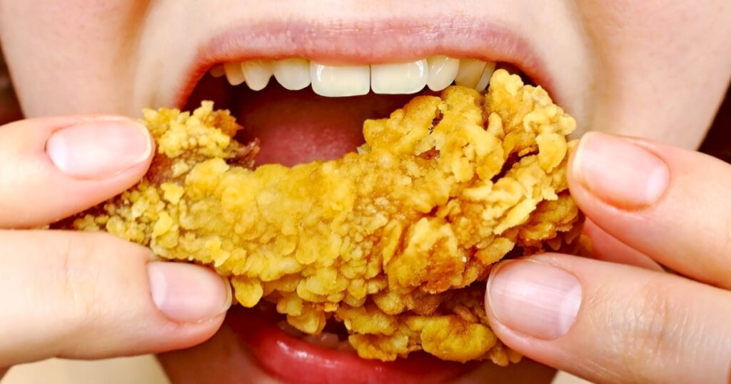 Woman eating a takeaway fried chicken wing from fast food cafe with a mouth and teeth close up