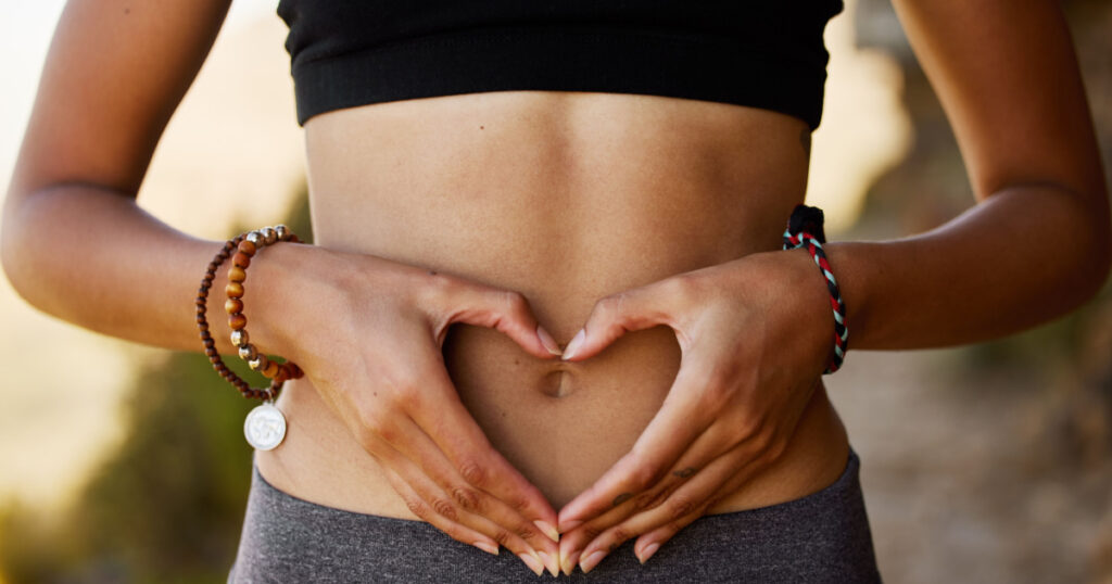 Woman, stomach and hand with heart in outdoor for exercise, diet, fitness and closeup. Female tummy, gut health and self love for wellness and training in the summer for healthy workout outside.