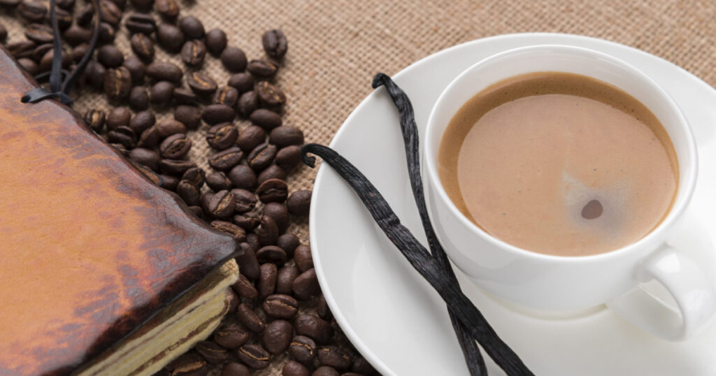 Delicious coffee in a white cup. Vanilla on the saucer. Coffee beans. Leather Notebook.
