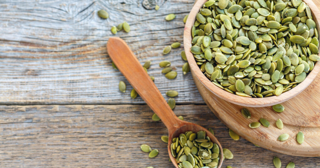 Bowl with pumpkin seeds and a wooden spoon on a wooden table.