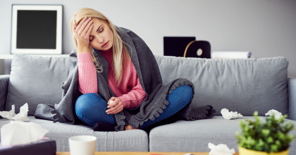 Sick woman with headache sitting under the blanket