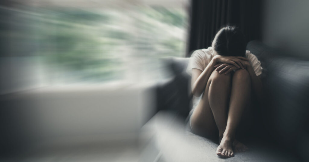 Depression and anxiety concept of woman in fetal position on the sofa with gloomy colors. Copy space.