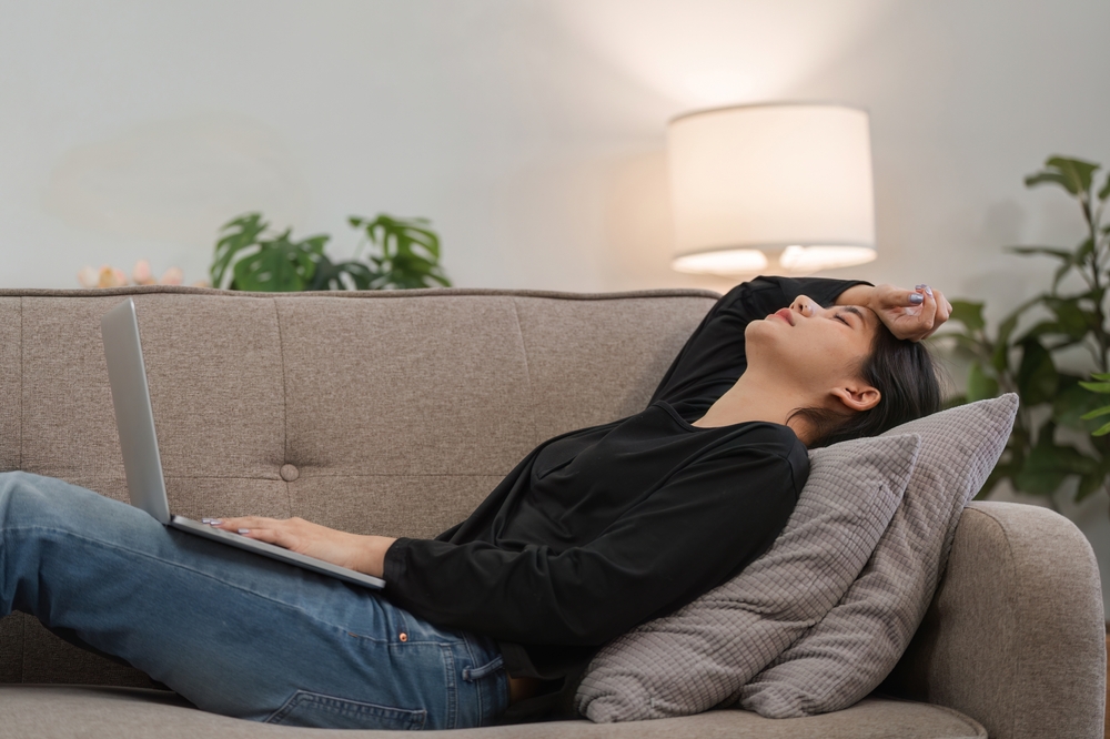 Young Woman Feeling Stressed and Overwhelmed at Work, Lying on Couch with Laptop, Experiencing Burnout and Fatigue