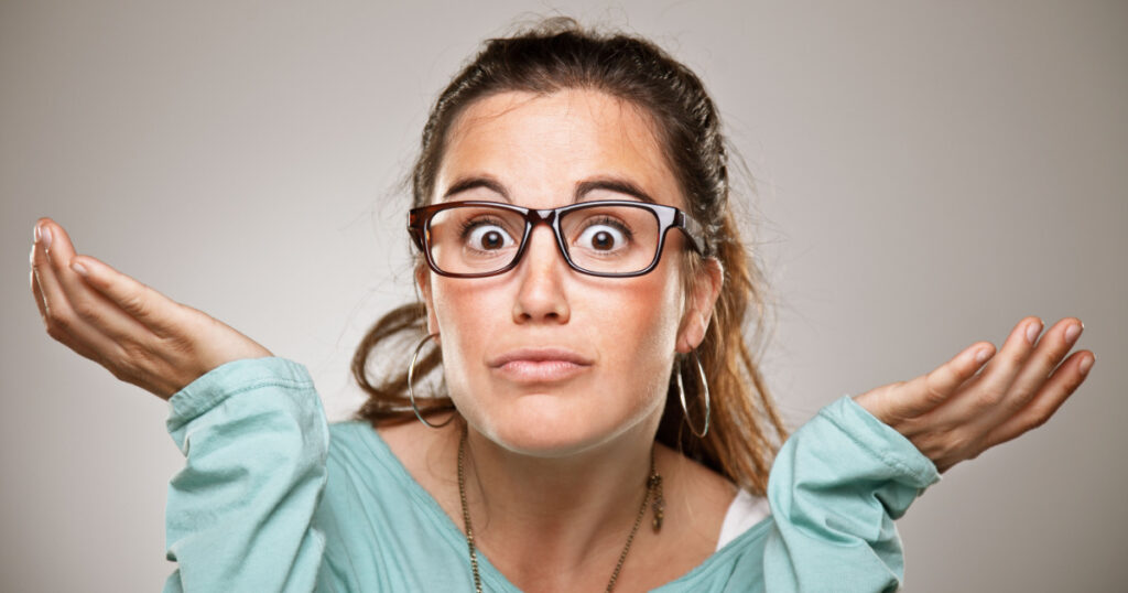 Shrugging woman in doubt doing shrug showing open palms. / Young woman portrait over grey background