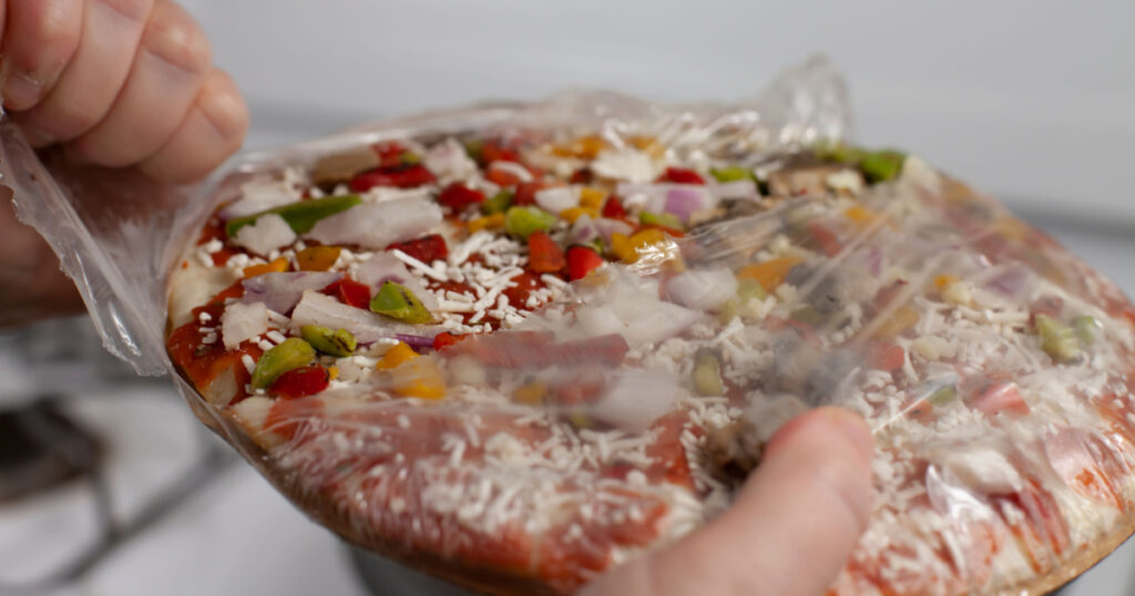 Hand opening a frozen pizza
