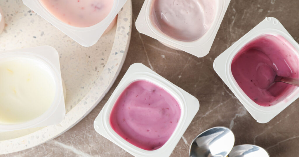 Composition with plastic cups with yogurt on grey table
