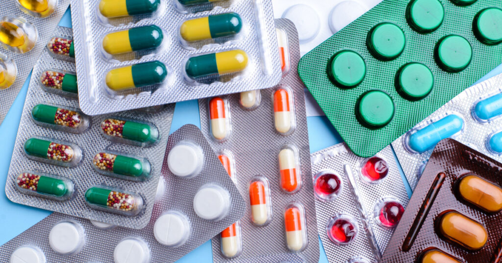 Different tablets, pills in foil blister packs, medications drugs on blue background