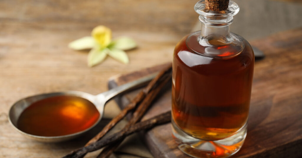 Aromatic homemade vanilla extract on wooden table, closeup.
