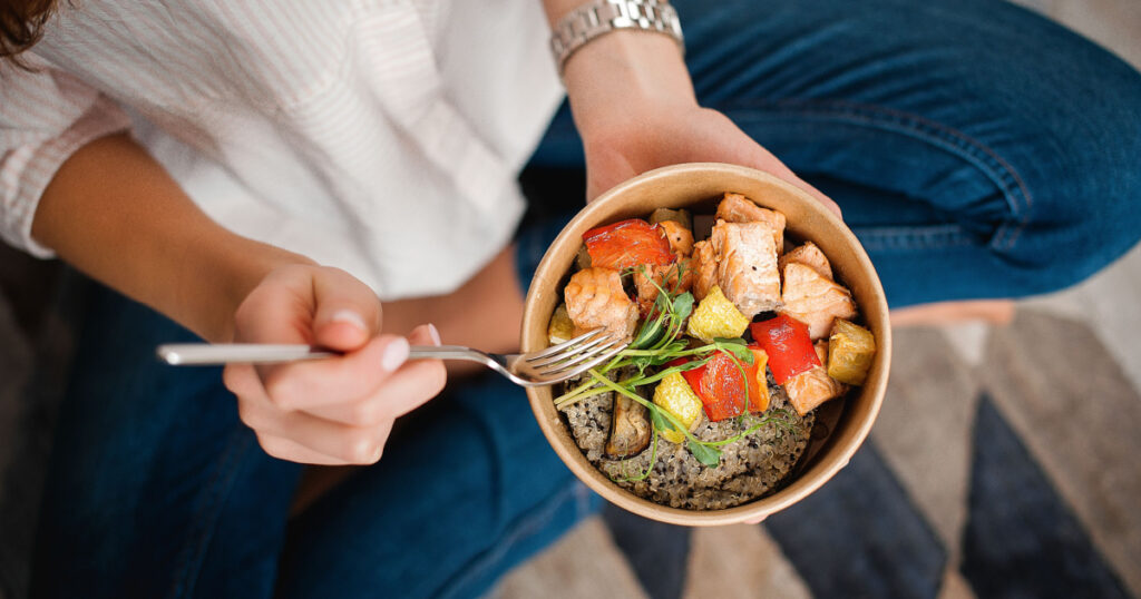Girl holds a paper plate with healthy food sitting on the floor. Home delivery food. Healthy eating concept. When you stay at home.
