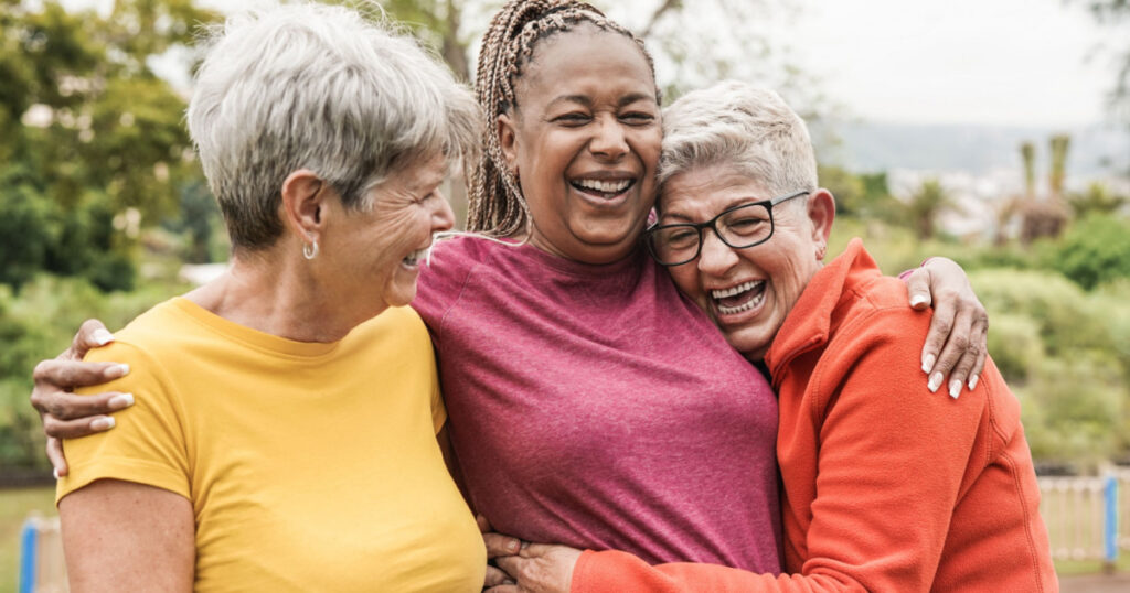 Happy multiracial senior women having fun together outdoor - Elderly generation people hugging each other at park