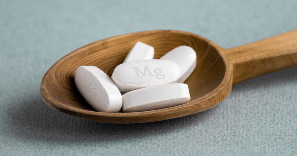 Tablets , vitamins with the abbreviation Mg ( magnesia, the macronutrient magnesium ) lying in a wooden spoon on a light background. Copy space.