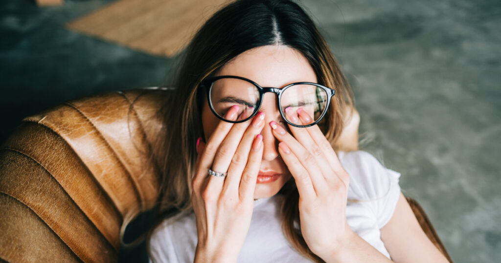 Young woman rubs her eyes after using glasses. Eye pain or fatigue concept.