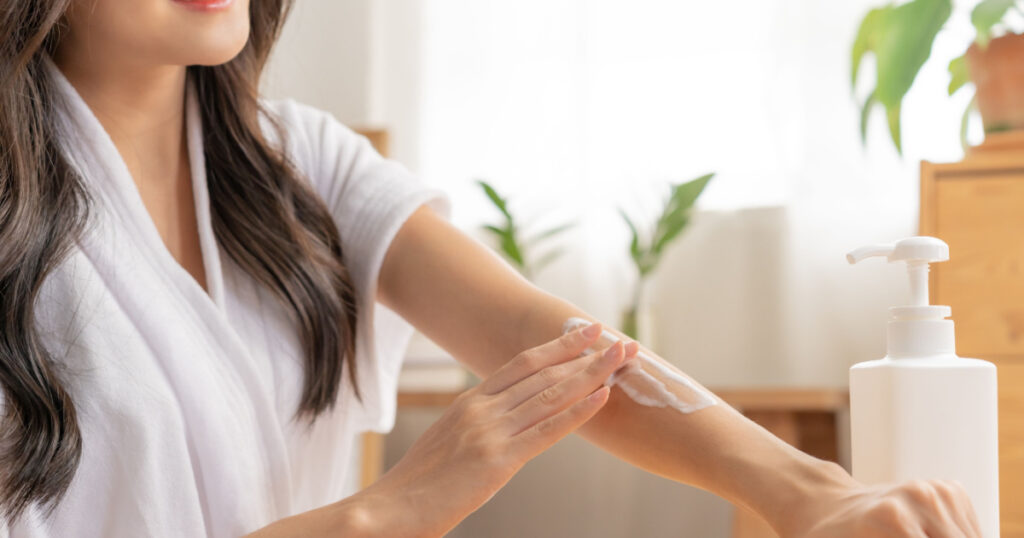 Healthy skin care, beauty asian young woman in bathrobe, towel after shower bath at home, hand in applying, putting moisturizer on her arm. Skin body cream moisturizing lotion, routine in the morning