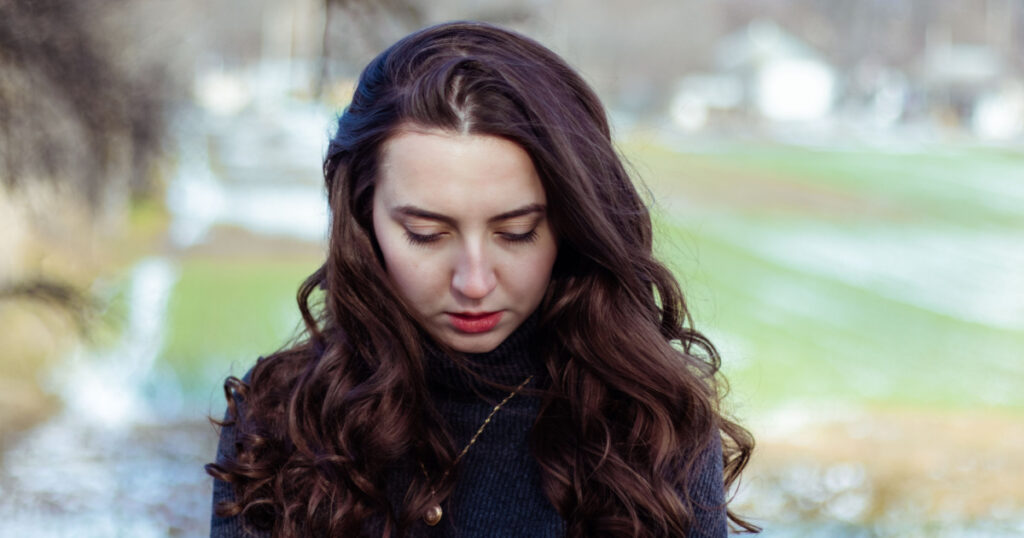 Sad woman.Girl in sadness.Portrait of a girl in nature.Beautiful curly hair.Woman looks down.Retro vintage colors.Vintage retouch.Feeling of loneliness.Winter portrait.Cold colors. Problems.Hair care.
