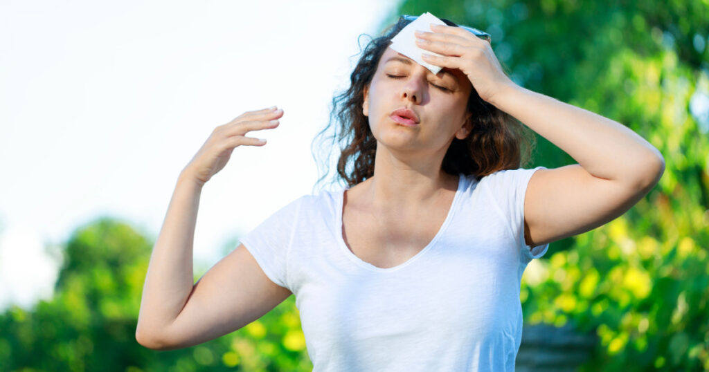 Young woman having hot flash and sweating in a warm summer day. Woman drying with paper napkin in too hot weather