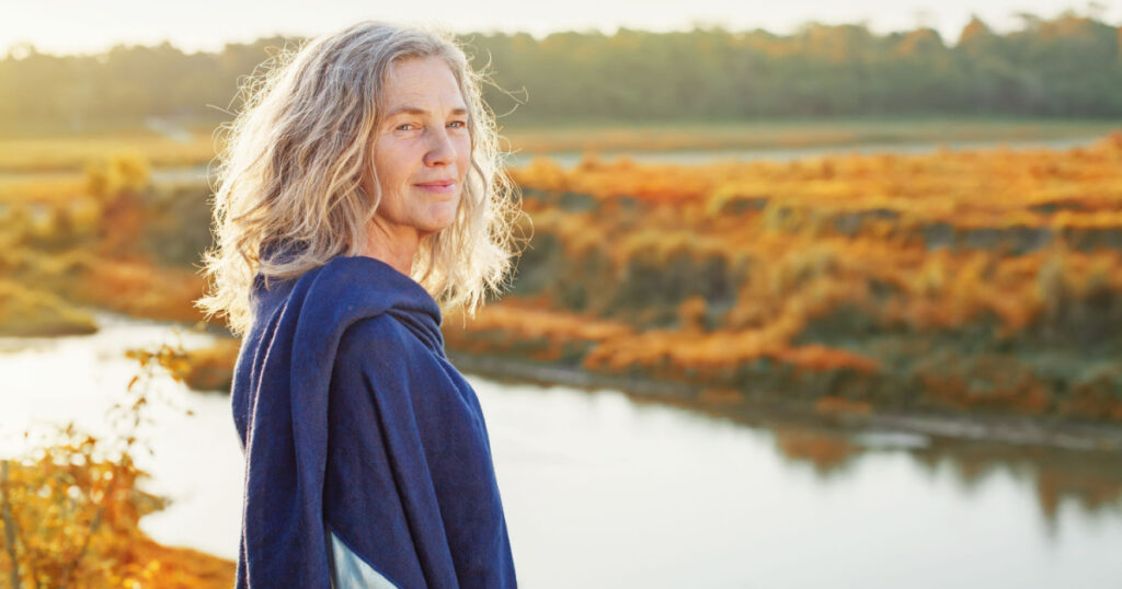 Beautiful mature woman standing in front of the river in autumn