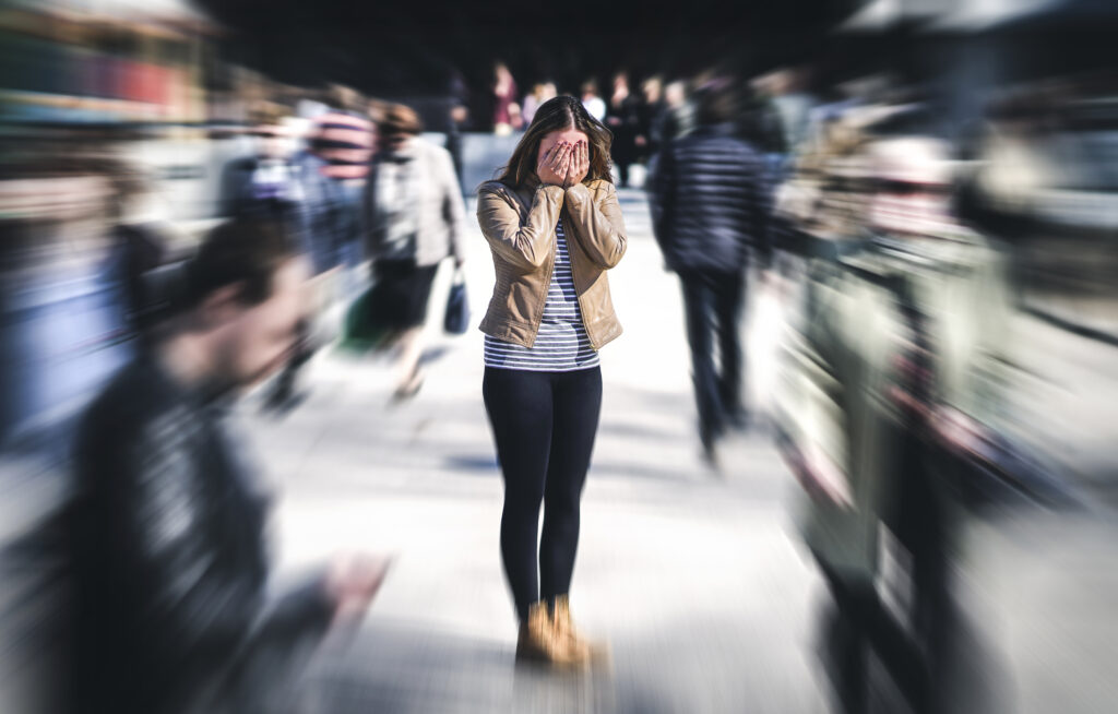 Panic attack in public place. Woman having panic disorder in city. Psychology, solitude, fear or mental health problems concept. Depressed sad person surrounded by people walking in busy street.
