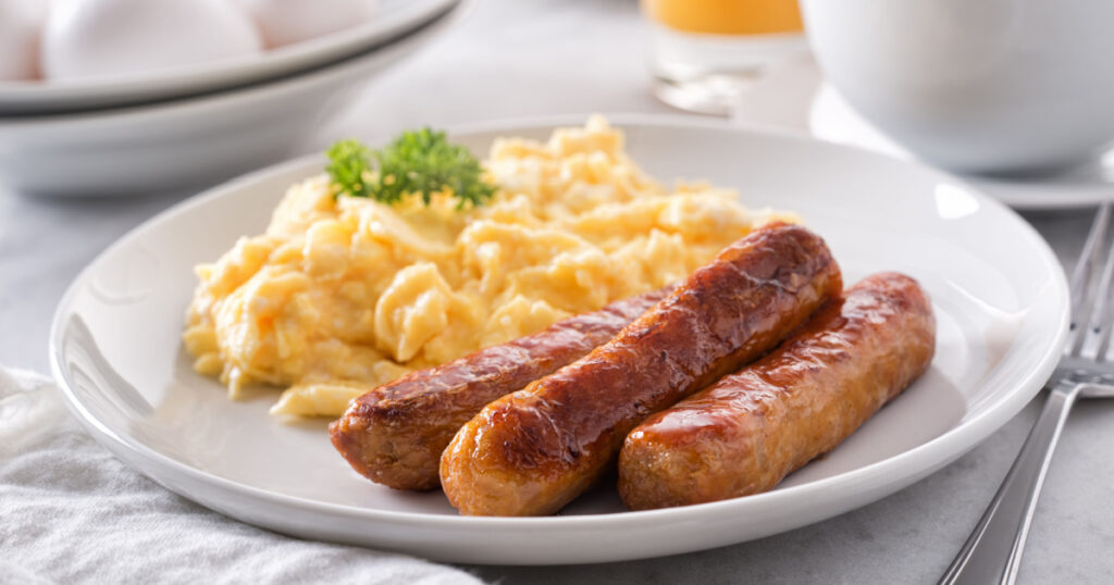A plate of delicious scrambled eggs and breakfast sausage with coffee and orange juice.