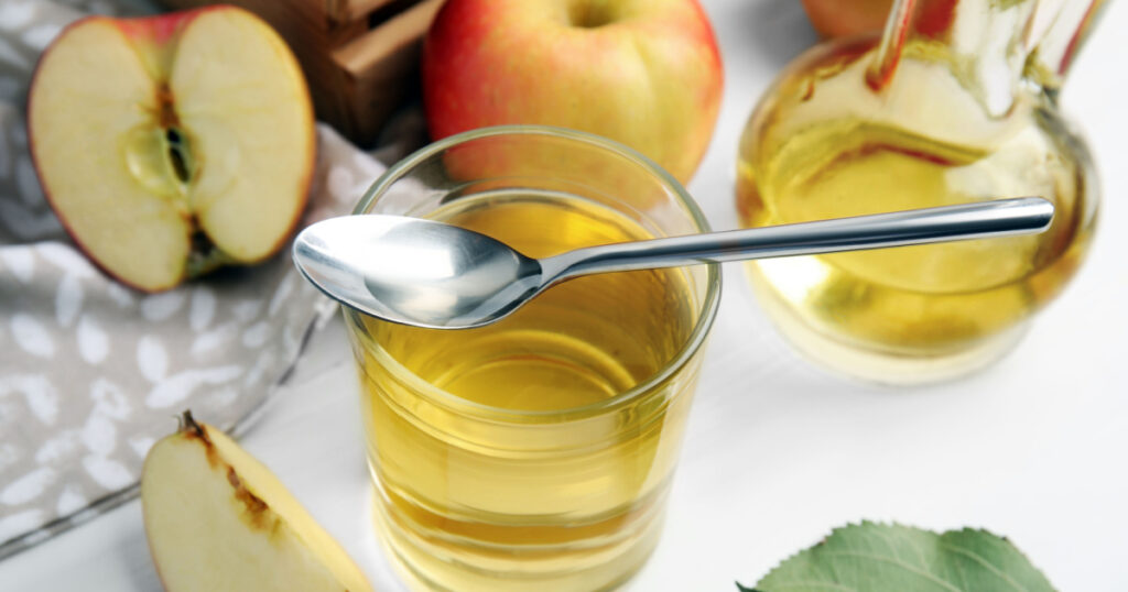 Natural apple vinegar and fresh fruits on white wooden table
