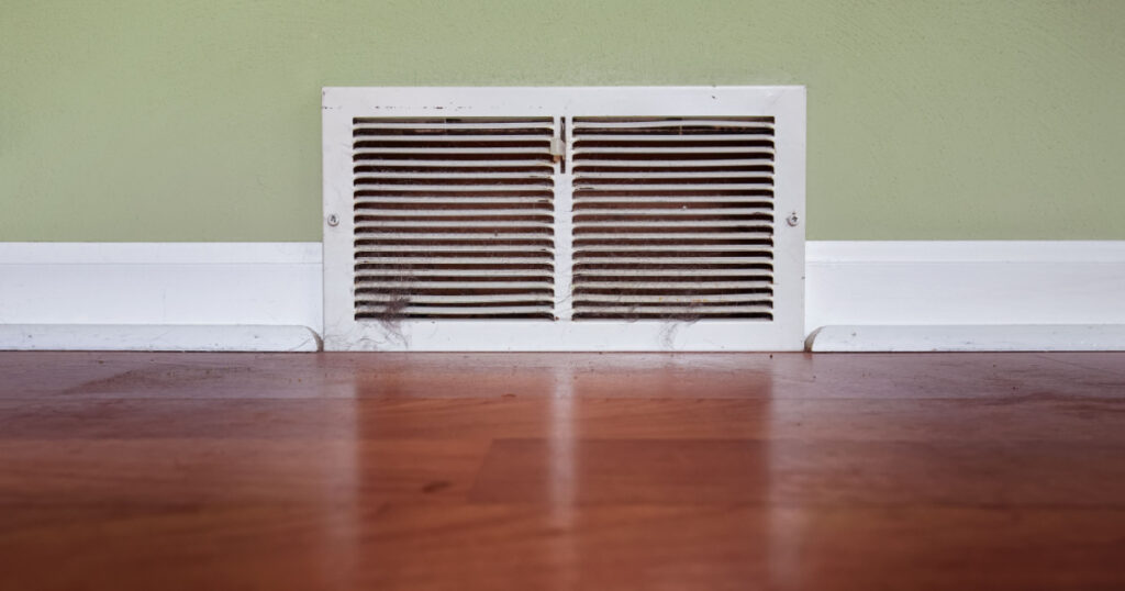 Dirty register wall vent with dust and pet hair clogging the duct opening in a home
