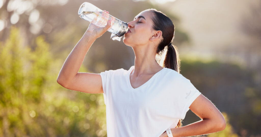 Drinking water, fitness and exercise woman after sports run and training in nature. Workout, hiking and walking challenge with a bottle of a female runner in summer ready for running for health