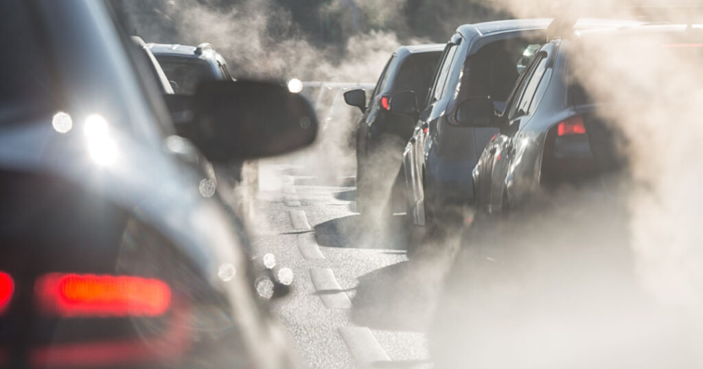 Blurred silhouettes of cars surrounded by steam from the exhaust pipes. Traffic jam
